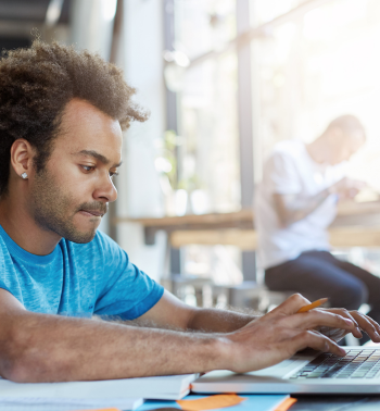 Man wearing a blue t-shirt sitting at a table on his laptop