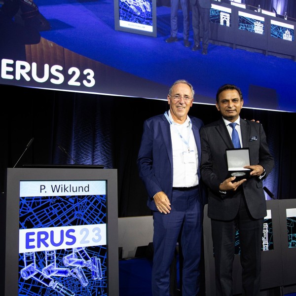 Prof Prokar Dasgupta on a stage holding the John Wickham Lifetime Achievement Award.